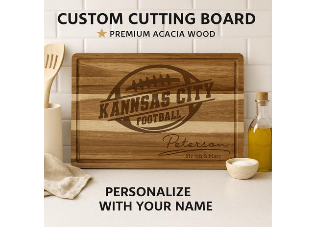 Custom acacia wood cutting board engraved with the words “Kansas City Football” inside a football logo, personalized below with the family name “Peterson” and “Steven & Mary.” The board is displayed upright on a white kitchen counter with a white tile backsplash, surrounded by kitchen utensils, a bottle of olive oil, and a small bowl of salt. Text above reads “CUSTOM CUTTING BOARD • PREMIUM ACACIA WOOD,” and below reads “PERSONALIZE WITH YOUR NAME.”