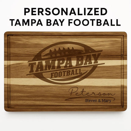 Personalized acacia wood cutting board engraved with a football logo and the text “Tampa Bay Football,” along with the family name “Peterson” and “Steven & Mary” in script at the bottom right. The board features natural striped wood grain and a carved juice groove, displayed against a white background with the words “PERSONALIZED TAMPA BAY FOOTBALL” above it.