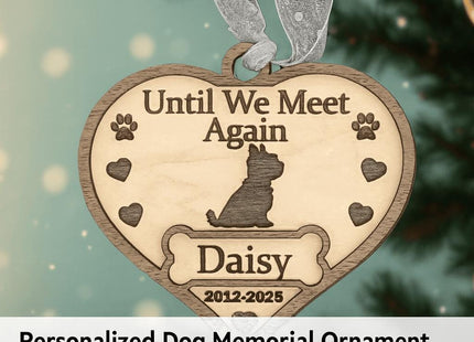 Heart-shaped wooden dog memorial ornament engraved with “Until We Meet Again,” featuring a dog silhouette, paw prints, hearts, and the name “Daisy” with dates “2012–2025.” The ornament hangs from a silver ribbon on a softly lit Christmas tree background. Text below reads “Personalized Dog Memorial Ornament – Custom Wooden Pet Loss Keepsake Gift.”