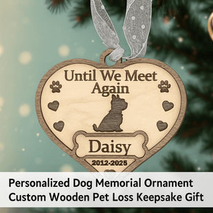 Heart-shaped wooden dog memorial ornament engraved with “Until We Meet Again,” featuring a dog silhouette, paw prints, hearts, and the name “Daisy” with dates “2012–2025.” The ornament hangs from a silver ribbon on a softly lit Christmas tree background. Text below reads “Personalized Dog Memorial Ornament – Custom Wooden Pet Loss Keepsake Gift.”