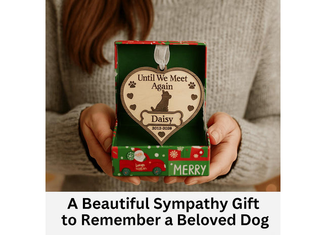 A woman holds an open festive gift box containing a personalized wooden dog memorial ornament engraved with “Until We Meet Again,” featuring a dog silhouette, paw prints, hearts, and the name “Daisy” with dates “2012–2028.” The box has a red and green Christmas design, and text below reads “A Beautiful Sympathy Gift to Remember a Beloved Dog.”