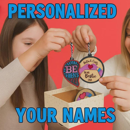 A woman and a young girl smile as they hold up personalized wooden best friend ornaments in front of a bright red holiday background. The woman holds a round ornament engraved with “Britta & Carly – In My Bestie Era,” while the girl holds a half-heart ornament labeled “BE FRIEN’S.” A decorative gift box sits on the table with more ornaments inside, and festive decorations like pine branches, candy canes, and ornaments line the left side. Blue text reads “PERSONALIZED YOUR NAMES.”