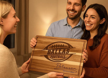 “Smiling couple receives a personalized Dallas Football acacia cutting board engraved with the name ‘Peterson – Steven & Mary’ as a housewarming gift from a friend. The warm indoor setting features soft lighting, creating a cozy and joyful atmosphere.”