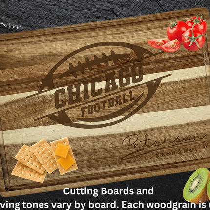 “Personalized Chicago football cutting board made from striped acacia wood, engraved with a football logo and the family name ‘Peterson – Steven & Mary.’ Board displayed on a dark slate surface with food items including tomatoes, crackers with cheese, and sliced kiwi. Text below reads ‘Cutting boards and engraving tones vary by board. Each woodgrain is unique.’”