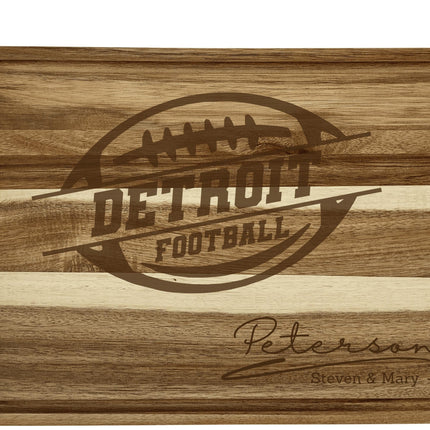“Personalized Detroit football cutting board crafted from acacia wood with light and dark striped grain. Engraved with a football logo and the family name ‘Peterson – Steven & Mary.’ Features a juice groove border and smooth finish, highlighting its quality craftsmanship and suitability as a gift for football fans.”