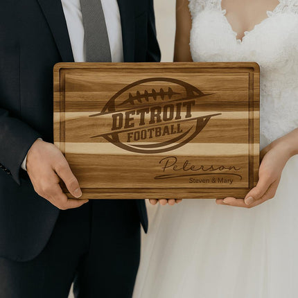 “Bride and groom holding a personalized Detroit football cutting board engraved with a football logo and the family name ‘Peterson – Steven & Mary.’ The acacia wood board features a striped grain pattern and juice groove, making it a unique and thoughtful wedding gift for football fans.”