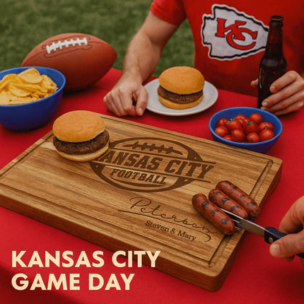 Alt text: Personalized acacia wood cutting board engraved with “Kansas City Football” and the name “Peterson – Steven & Mary,” displayed on a red tablecloth during a Kansas City football game day cookout. The scene includes burgers, grilled sausages, a bowl of chips, cherry tomatoes, a football, and fans wearing red Kansas City shirts. Text in the bottom left corner reads “KANSAS CITY GAME DAY.”