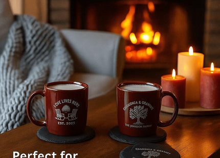 “Cozy living room scene with two red mugs of hot drinks resting on personalized slate coasters in front of a warm fireplace. One coaster reads ‘Love Lives Here – Est. 2025’ and the other ‘Grandma & Grandpa – The Johnson Family.’ Candles and a soft blanket complete the inviting atmosphere. Text on image says ‘Perfect for Family Gatherings.’”