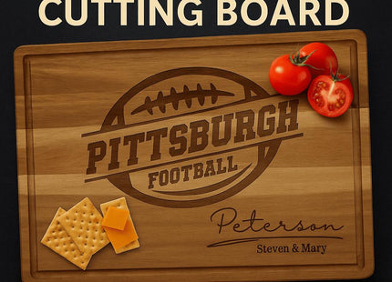 Personalized acacia wood cutting board engraved with a football design and the text “Pittsburgh Football.” Below, it features the family name “Peterson” in elegant script with “Steven & Mary” engraved underneath. The board has a juice groove around the edge and is styled with sliced tomatoes and cheese crackers for a warm, rustic presentation.