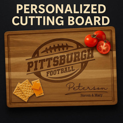Personalized acacia wood cutting board engraved with a football design and the text “Pittsburgh Football.” Below, it features the family name “Peterson” in elegant script with “Steven & Mary” engraved underneath. The board has a juice groove around the edge and is styled with sliced tomatoes and cheese crackers for a warm, rustic presentation.