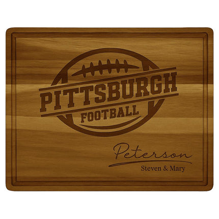 Personalized acacia wood cutting board engraved with the text “Pittsburgh Football” and a football graphic in the center. The bottom right corner features the family name “Peterson” in elegant script with “Steven & Mary” engraved below. The board has a smooth finish with a beveled juice groove around the edge, highlighting its craftsmanship and rich wood grain.
