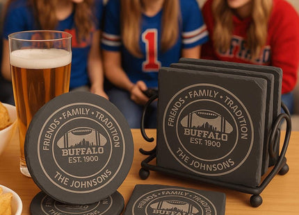 &quot;Buffalo-themed personalized slate coasters displayed on a wooden table with snacks and drinks. The coasters are engraved with &#39;Friends • Family • Tradition,&#39; &#39;Buffalo Est. 1900,&#39; and &#39;The Johnsons.&#39; A glass of beer and bowls of chips sit nearby, with three women in Buffalo team shirts laughing together in the background, creating a fun game-day atmosphere.&quot;
