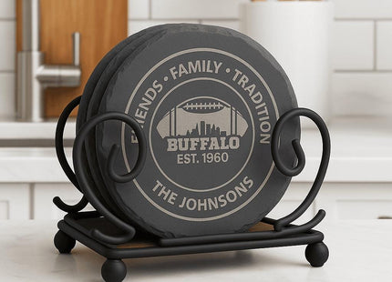 &quot;Set of round black slate coasters displayed in a decorative black iron holder on a white kitchen countertop. Each coaster is engraved with &#39;Friends • Family • Tradition,&#39; &#39;Buffalo Est. 1960,&#39; and &#39;The Johnsons,&#39; featuring a football and city skyline design.&quot;