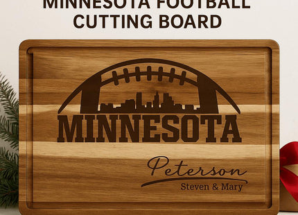 &quot;Personalized Minnesota football cutting board made of striped acacia wood with engraved football and city skyline design. The engraving reads &#39;MINNESOTA&#39; with the family name &#39;Peterson&#39; and &#39;Steven & Mary&#39; below. Displayed with a small cheese knife and red ribbon, set against a clean neutral background with evergreen accents.&quot;