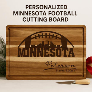 &quot;Personalized Minnesota football cutting board made of striped acacia wood with engraved football and city skyline design. The engraving reads &#39;MINNESOTA&#39; with the family name &#39;Peterson&#39; and &#39;Steven & Mary&#39; below. Displayed with a small cheese knife and red ribbon, set against a clean neutral background with evergreen accents.&quot;