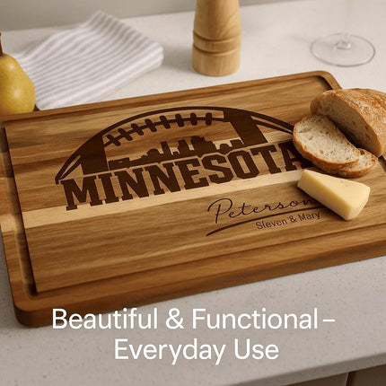 "Personalized Minnesota football cutting board made of acacia wood, engraved with a football and skyline design and the name 'Peterson – Steven & Mary.' The board is shown on a kitchen counter with sliced bread, a wedge of cheese, and a pear nearby. Text overlay reads 'Beautiful & Functional – Everyday Use.'"