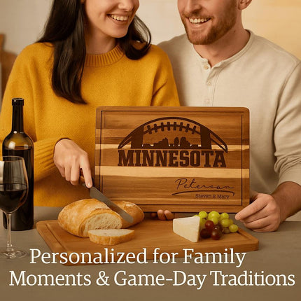 "Smiling couple enjoying wine and bread at a cozy table, holding a personalized Minnesota football cutting board engraved with a football and skyline design and the names 'Peterson – Steven & Mary.' The board is displayed with sliced bread, cheese, and grapes. Text overlay reads 'Personalized for Family Moments & Game-Day Traditions.'"