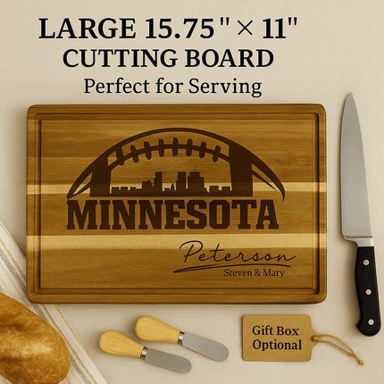 "Personalized Minnesota football cutting board made of acacia wood, engraved with a football and skyline design and the name 'Peterson – Steven & Mary.' The board measures 15.75 by 11 inches and is shown with bread, a large knife, and two small cheese spreaders. A gift tag reads 'Gift Box Optional.' Text overlay reads 'Large 15.75" × 11" Cutting Board – Perfect for Serving.'"