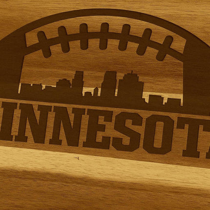 "Close-up view of a laser-engraved Minnesota football design on an acacia wood cutting board, featuring a football outline with a city skyline and the word 'MINNESOTA' engraved below."