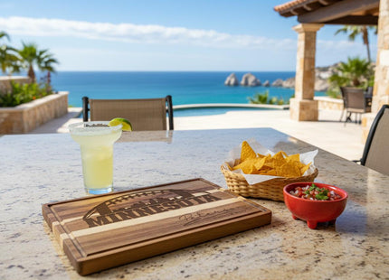 &quot;Personalized Minnesota football cutting board engraved with a football and skyline design sits on an outdoor stone table overlooking a scenic ocean view. Next to it are a basket of tortilla chips, a red bowl of salsa, and a margarita with a lime wedge, creating a relaxed coastal entertaining scene.&quot;