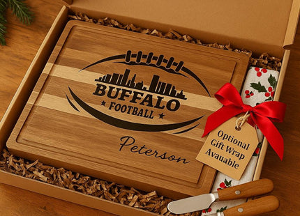 &quot;Personalized Buffalo Football cutting board engraved with skyline and football design, featuring the name &#39;Peterson,&#39; displayed inside a gift box with shredded paper filler. The box includes two cheese spreader knives and a festive towel with holly pattern tied with a red bow and gift tag reading &#39;Optional Gift Wrap Available.&#39; Text on image says &#39;Ready to Give&#39; and &#39;Optional Gift Wrap Available.&#39;&quot;