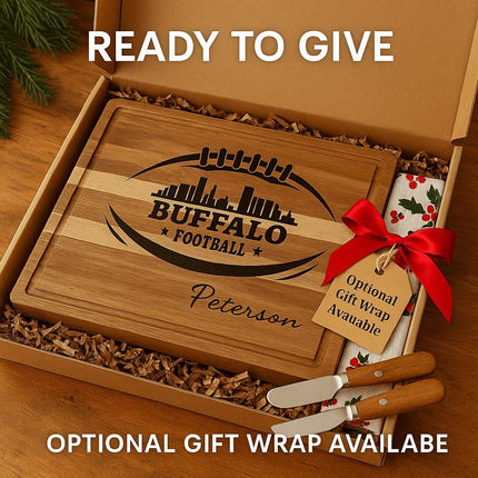"Personalized Buffalo Football cutting board engraved with skyline and football design, featuring the name 'Peterson,' displayed inside a gift box with shredded paper filler. The box includes two cheese spreader knives and a festive towel with holly pattern tied with a red bow and gift tag reading 'Optional Gift Wrap Available.' Text on image says 'Ready to Give' and 'Optional Gift Wrap Available.'"