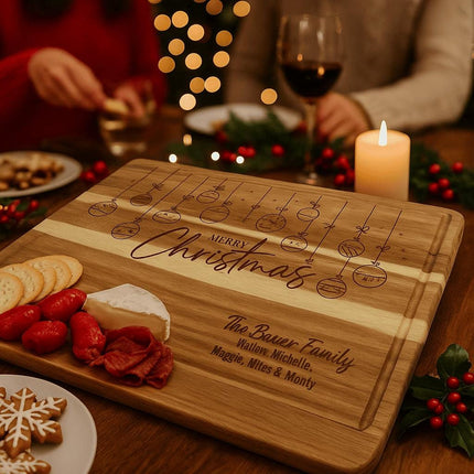 Personalized acacia cutting board engraved with hanging Christmas ornaments and the words “Merry Christmas” and “The Bauer Family” is displayed as a holiday charcuterie board with crackers, cheese, and meats, surrounded by candles, holly decor, and people enjoying food and wine in a festive setting.