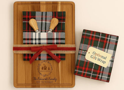 : Personalized acacia cutting board holiday gift set displayed with a plaid holiday towel, two wooden spreader knives, and a red ribbon bow wrapped around the board. Next to it is a matching plaid gift-wrapped box with a tag that reads “Optional Gift Wrap.” The engraving on the board shows a family name and holiday design. Text above reads “COMPLETE HOLIDAY GIFT SET,” and below lists the contents: “Custom Board • Holiday Towel • 2 Spreaders • Optional Gift Wrap.”