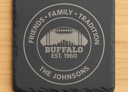&quot;Square black slate coaster engraved with a Buffalo football design featuring the text &#39;Friends • Family • Tradition,&#39; &#39;Buffalo Est. 1960,&#39; and &#39;The Johnsons.&#39; The engraving shows a football silhouette with a city skyline inside, displayed on a light wood background.&quot;
