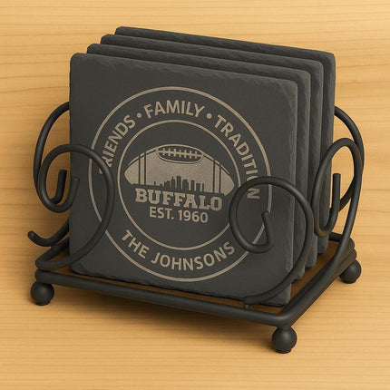 "Set of four square black slate coasters engraved with a Buffalo football design displayed in a black wrought iron holder. The coasters feature the text 'Friends • Family • Tradition,' 'Buffalo Est. 1960,' and 'The Johnsons.' The holder has decorative scrollwork and sits on a light wooden surface."
