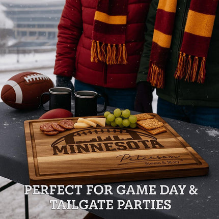 "Personalized Minnesota football cutting board displayed at a snowy tailgate party with grapes, cheese, crackers, and salami on top. Two people wearing winter coats and maroon-and-gold scarves stand behind the table with mugs and a football nearby. Text overlay reads 'Perfect for Game Day & Tailgate Parties.'"