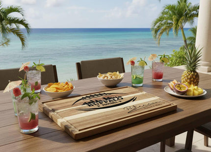 &quot;Personalized Buffalo Football cutting board with engraved football and skyline design and the name &#39;Peterson – Steven & Mary,&#39; displayed on an outdoor table overlooking a tropical ocean view. The table is set with colorful tropical drinks, bowls of chips and nuts, and a plate of pineapple and passion fruit, creating a relaxed beachside entertaining scene.&quot;