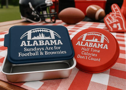 &quot;Two personalized Alabama football-themed bakeware pieces — a navy blue rectangular cake pan engraved with &#39;Sundays Are for Football & Brownies&#39; and a red round pie tin engraved with &#39;Half Time Calories Don’t Count&#39; — displayed on a red and white checkered picnic tablecloth. A football helmet, foam finger, footballs, and a cooler sit in the background, emphasizing the tailgate setting. Text at the bottom reads &#39;Football & Team Spirit Themes – For families or fans.&#39;&q