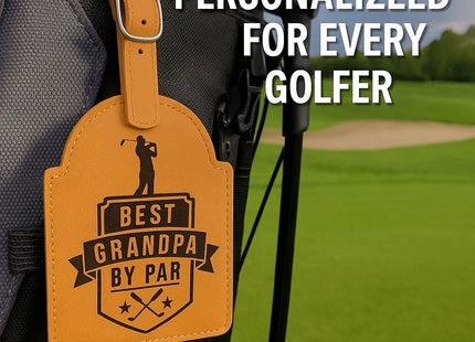 &quot;Tan leather golf bag tag engraved with the phrase &#39;Best Grandpa by Par&#39; featuring a golfer silhouette and crossed golf clubs, attached to a black and gray golf bag. The bag rests on a lush green golf course with a sand trap in the background. Text at the top reads &#39;Personalized for Every Golfer.&#39;&quot;