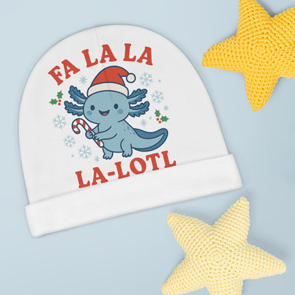 “White baby beanie with a blue cartoon axolotl wearing a Santa hat and holding a candy cane. The text ‘FA LA LA LA-LOTL’ is printed in red above and below the character. The beanie is displayed on a light blue background with two knitted yellow star plush toys.”