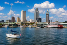 Mobile Alabama harbor with Gulf Coast marina, sailboats, waterfront docks, and historic southern skyline beneath a warm coastal sunset.