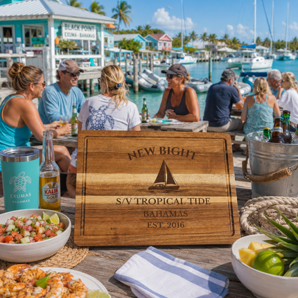New Bight Bahamas sailboat cutting board displayed beside a peaceful tropical anchorage with calm turquoise water and distant sailboats on Cat Island