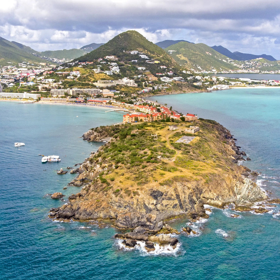 Aerial view of the Philipsburg peninsula and Great Bay in Sint Maarten featuring turquoise Caribbean waters, coastal development, surrounding hills, and harbor approaches