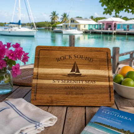 Rock Sound Bahamas sailboat cutting board displayed at a quiet dockside harbor setting with calm turquoise water and anchored sailboats in Eleuthera