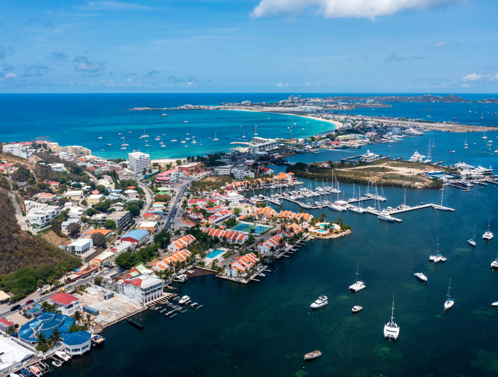 Aerial view of Simpson Bay Lagoon in Saint Martin showing sailboats, marinas, turquoise Caribbean waters, and the lagoon entrance.