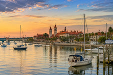 Sunset view of St. Augustine Harbor featuring sailboats, calm marina waters, historic waterfront architecture, palm trees, and the iconic twin towers of the city skyline along Florida’s Atlantic coast.