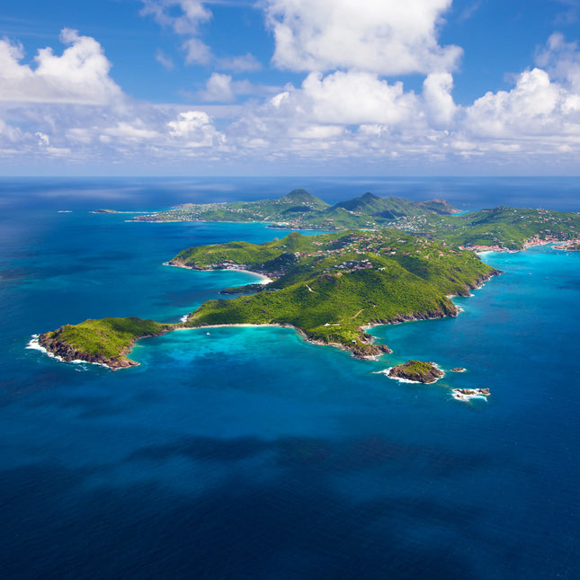 Aerial view of St. Barths showing the island's coastline, turquoise bays, rolling hills, and surrounding Caribbean waters.
