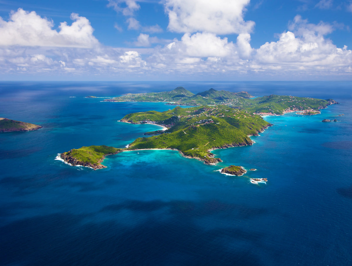 Aerial view of St. Barths showing the island's coastline, turquoise bays, rolling hills, and surrounding Caribbean waters.