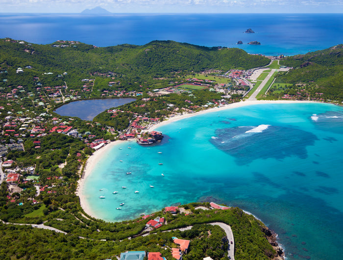 Aerial view of St. Jean Bay in St. Barths featuring turquoise waters, white sand beaches, anchored sailboats, Eden Rock, and the famous Gustaf III Airport runway.