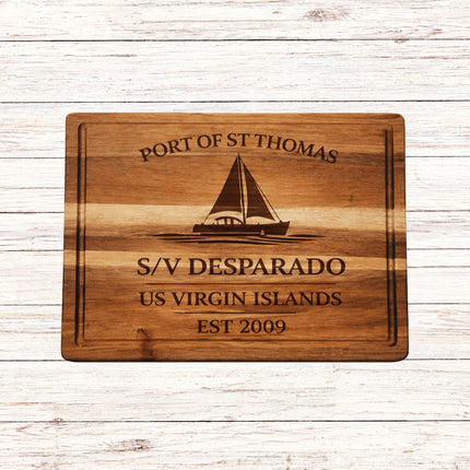 Wooden cutting board with engraved text and sailboat design on a wooden surface