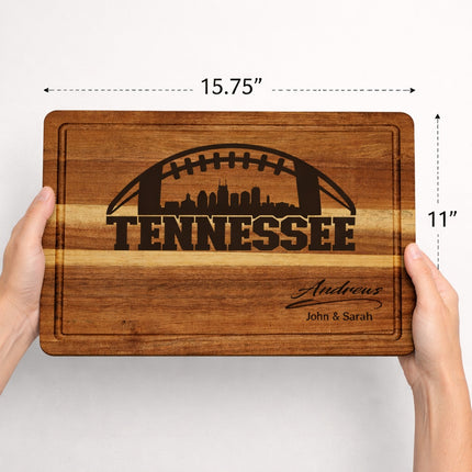 Tennessee football cutting board shown in hands for size reference, measures 15.75 x 11 x 1 inches, solid acacia wood with laser engraved skyline and personalized family name
