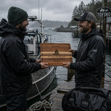 Tofino British Columbia personalized cutting board being handed between sailors on a rain soaked dock with boats and rugged coastline in the background