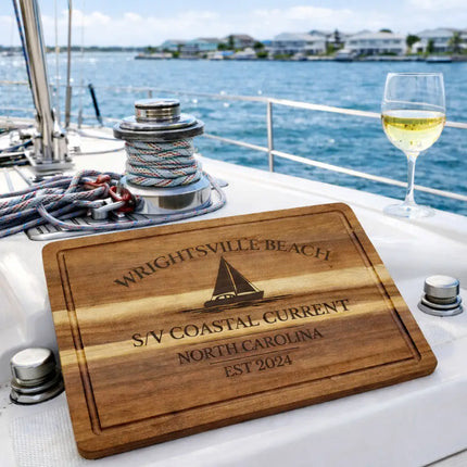 Wrightsville Beach personalized cutting board displayed on a sailboat deck with ocean view and coastal homes in background